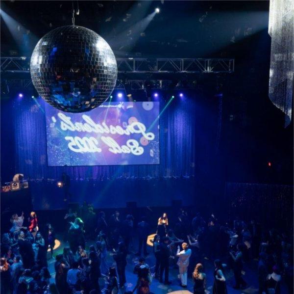 An above shot of a room full of Lakers dancing. A sign hanging reads Presidents� Ball 2025. A large silver disco ball hangs from the ceiling.